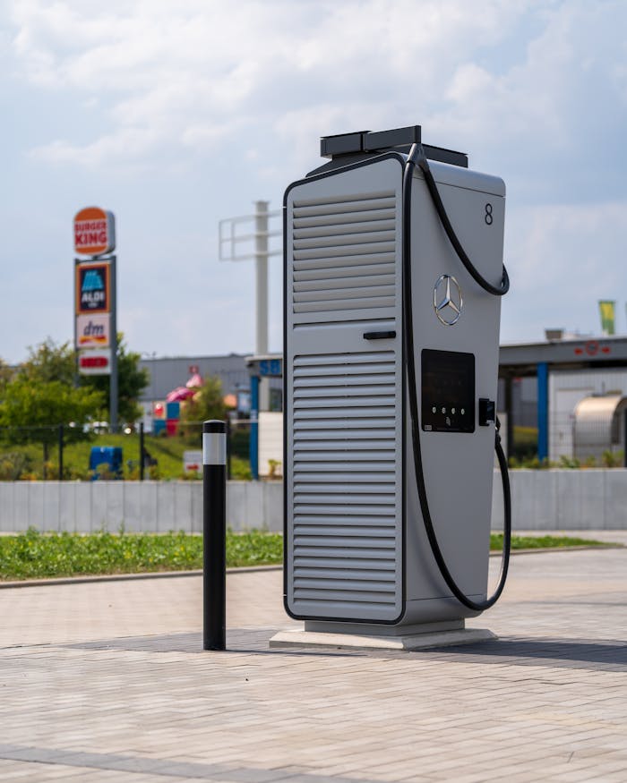 Electric vehicle charging station at a commercial area with visible fast-food and retail signs under a cloudy sky.